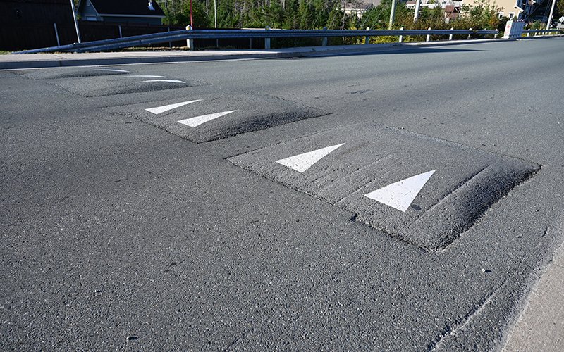 Four square raised asphalt humps that have spaces between them and marked by white triangle markers indicating direction of travel